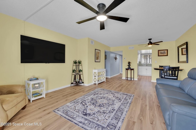 living area featuring a ceiling fan, visible vents, light wood-type flooring, and baseboards