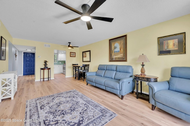 living area featuring visible vents, baseboards, a textured ceiling, and light wood-style flooring