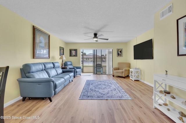 living area with visible vents, a textured ceiling, light wood-style floors, and a ceiling fan