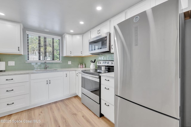 kitchen with light wood-type flooring, a sink, stainless steel appliances, white cabinets, and decorative backsplash