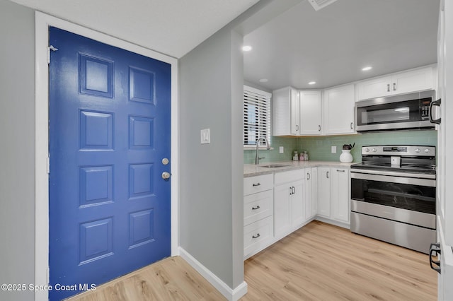 kitchen featuring light wood finished floors, decorative backsplash, white cabinets, stainless steel appliances, and a sink