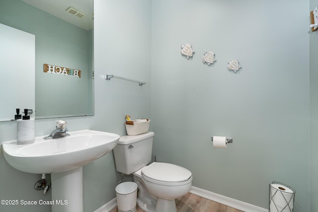 half bathroom with toilet, a sink, visible vents, wood finished floors, and baseboards