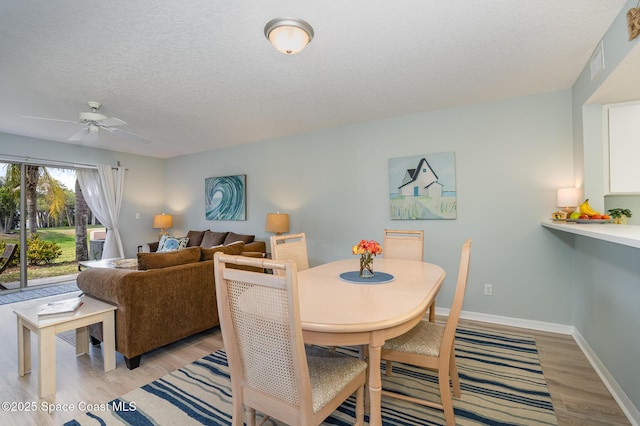 dining space featuring a textured ceiling, ceiling fan, visible vents, baseboards, and light wood-type flooring