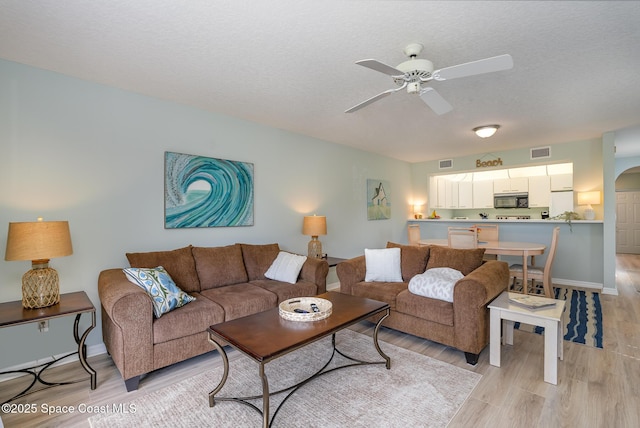 living room featuring a textured ceiling, arched walkways, visible vents, a ceiling fan, and light wood-type flooring