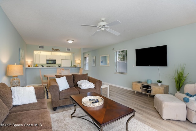 living area with a textured ceiling, visible vents, baseboards, a ceiling fan, and light wood-type flooring