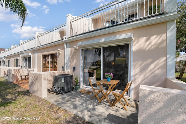 rear view of house with a patio, stucco siding, a balcony, and central air condition unit