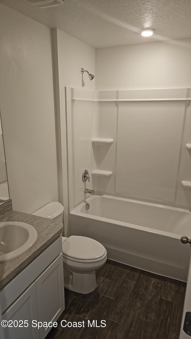 full bath with toilet, a textured ceiling, wood finished floors, bathtub / shower combination, and vanity