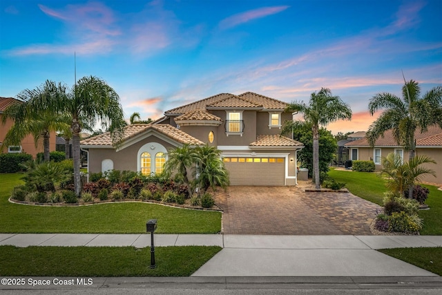 mediterranean / spanish house with stucco siding, driveway, a garage, a yard, and a tiled roof