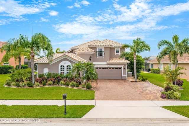mediterranean / spanish home featuring stucco siding, decorative driveway, an attached garage, a front yard, and a tile roof