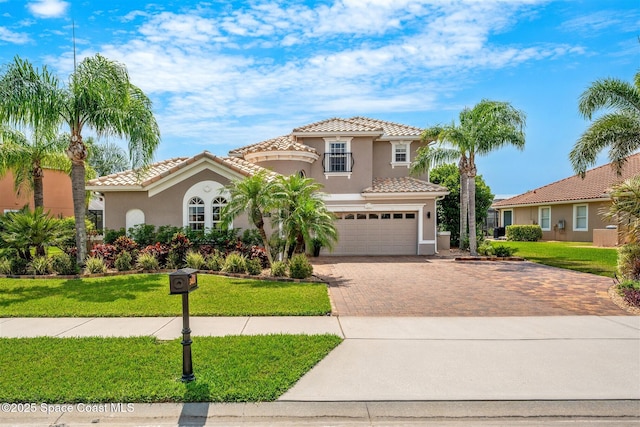 mediterranean / spanish house featuring stucco siding, a tiled roof, decorative driveway, and a front lawn