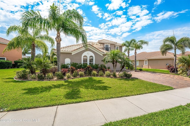 mediterranean / spanish house with stucco siding, a front yard, a tile roof, and decorative driveway