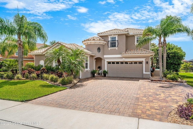 mediterranean / spanish-style house with a tile roof, a garage, decorative driveway, and stucco siding