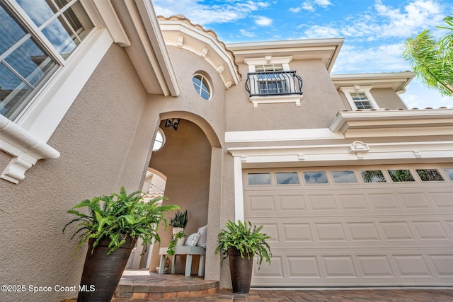 property entrance with a balcony, driveway, and stucco siding