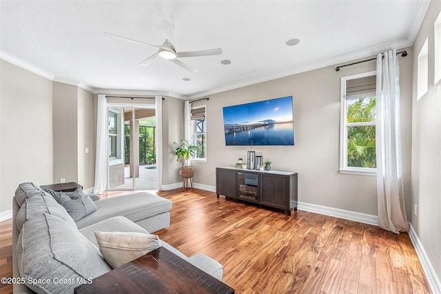 living room with ornamental molding, light wood-style flooring, ceiling fan, and baseboards