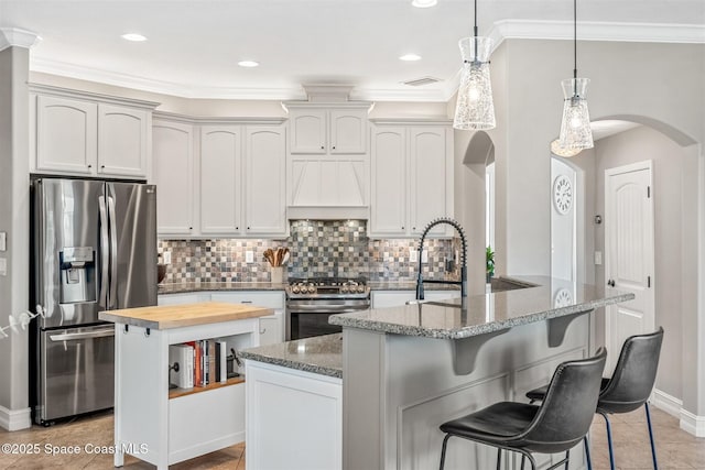kitchen featuring butcher block countertops, visible vents, arched walkways, appliances with stainless steel finishes, and custom range hood