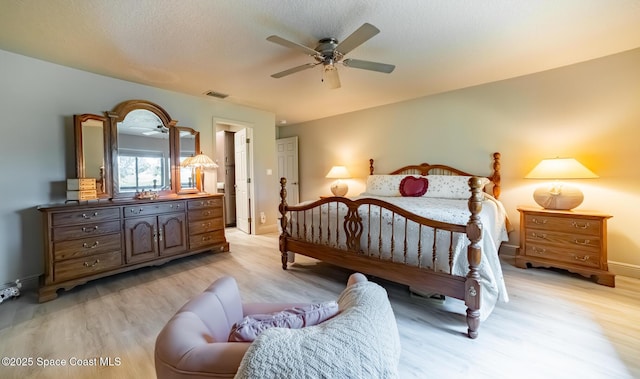 bedroom featuring light wood finished floors, ceiling fan, visible vents, and a textured ceiling