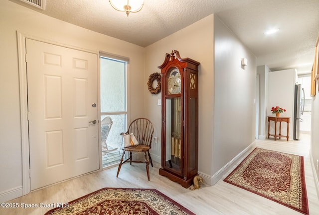 entrance foyer featuring a textured ceiling, wood finished floors, visible vents, and baseboards