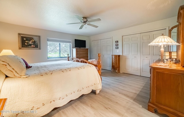 bedroom featuring ceiling fan, light wood-style flooring, a textured ceiling, and two closets