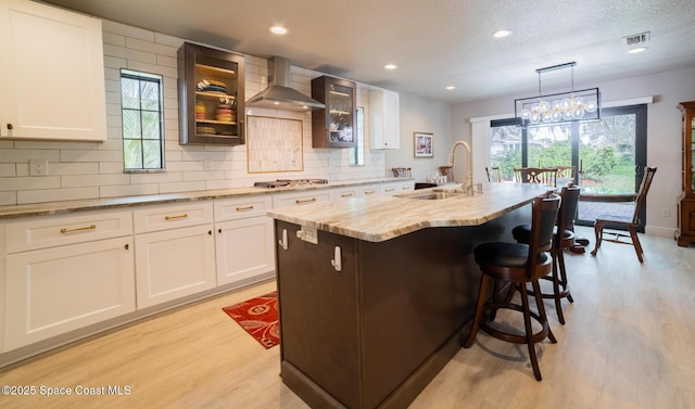 kitchen featuring visible vents, white cabinets, light wood-type flooring, wall chimney range hood, and backsplash