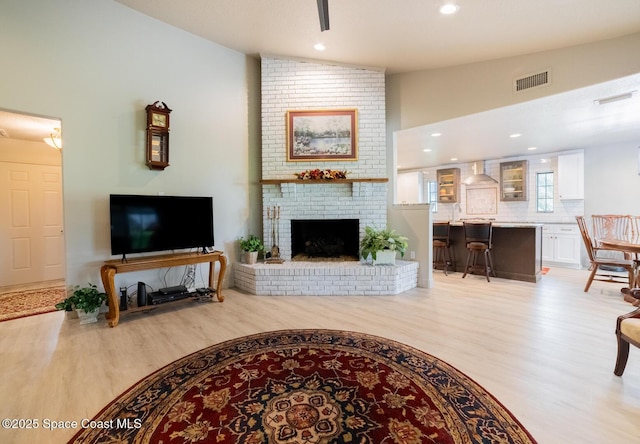 living area with light wood-style floors, lofted ceiling, a brick fireplace, and visible vents