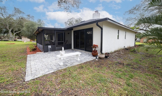 back of property with a patio, a sunroom, a chimney, a yard, and stucco siding