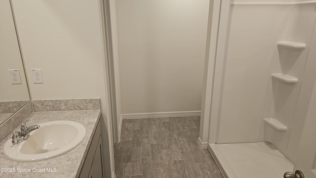 bathroom with wood finish floors, baseboards, walk in shower, and vanity