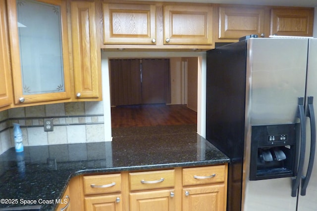 kitchen featuring dark stone countertops, stainless steel refrigerator with ice dispenser, and decorative backsplash