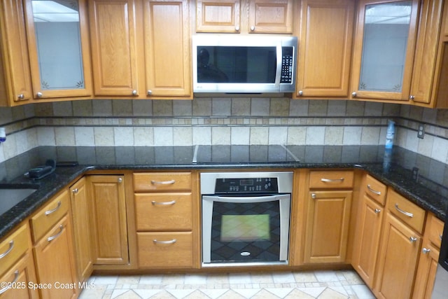 kitchen featuring appliances with stainless steel finishes, brown cabinetry, backsplash, and dark stone countertops