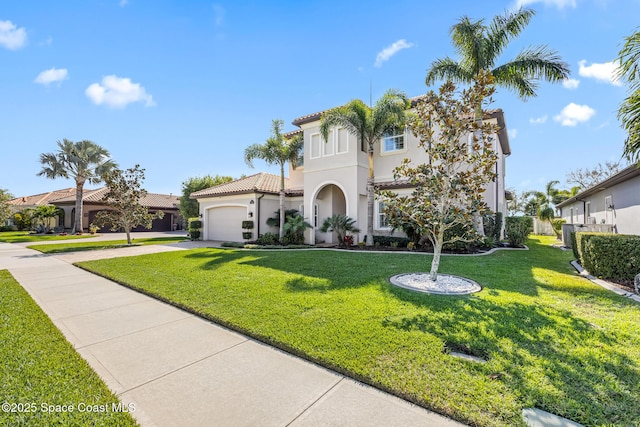 mediterranean / spanish house with a tile roof, stucco siding, an attached garage, a front yard, and driveway