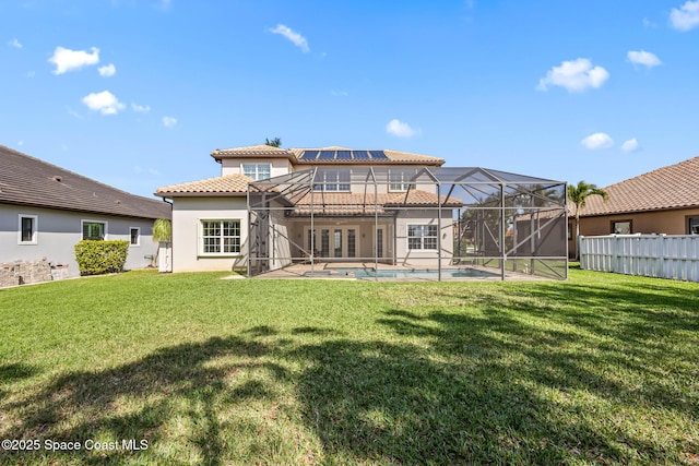 rear view of property featuring glass enclosure, a lawn, a fenced in pool, and stucco siding