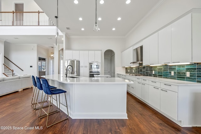 kitchen with stainless steel appliances, a spacious island, a sink, wall chimney range hood, and backsplash