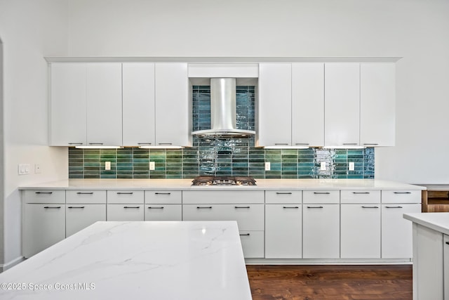 kitchen with tasteful backsplash, stainless steel gas stovetop, dark wood-type flooring, light stone countertops, and wall chimney exhaust hood