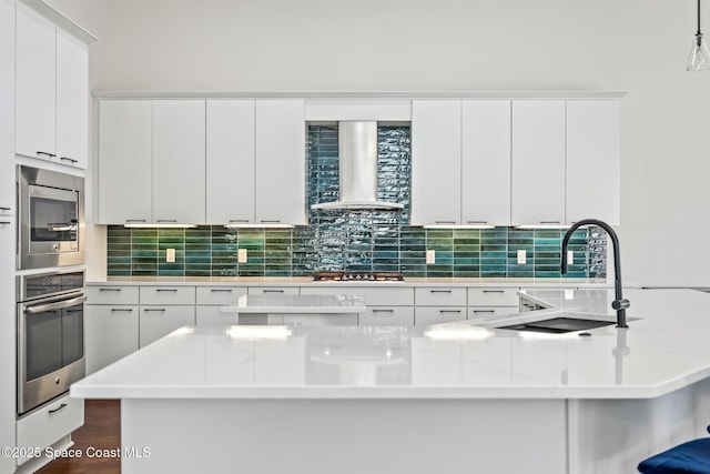 kitchen with tasteful backsplash, white cabinets, wall chimney range hood, and appliances with stainless steel finishes