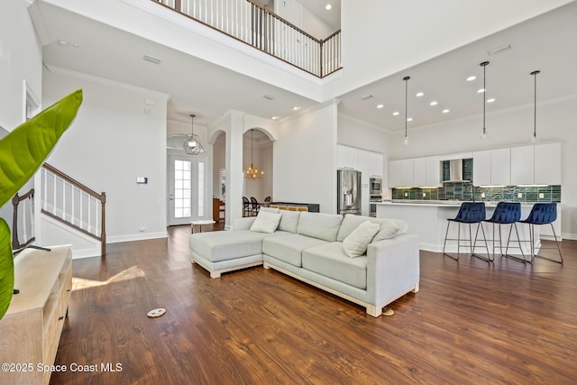 living area with arched walkways, stairs, a towering ceiling, and dark wood-style floors