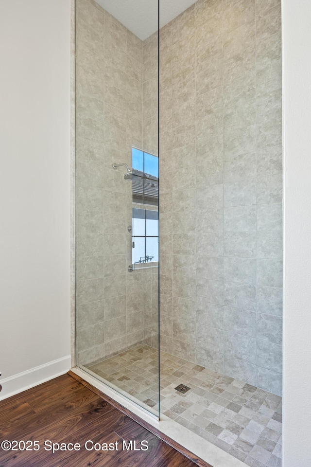 full bathroom featuring baseboards, a tile shower, and wood finished floors