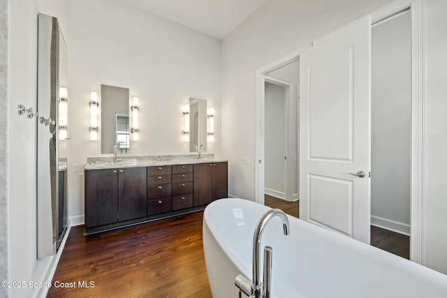 bathroom with double vanity, a soaking tub, a sink, wood finished floors, and baseboards