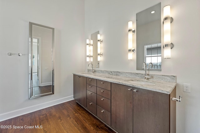 full bath featuring double vanity, wood finished floors, a sink, and baseboards