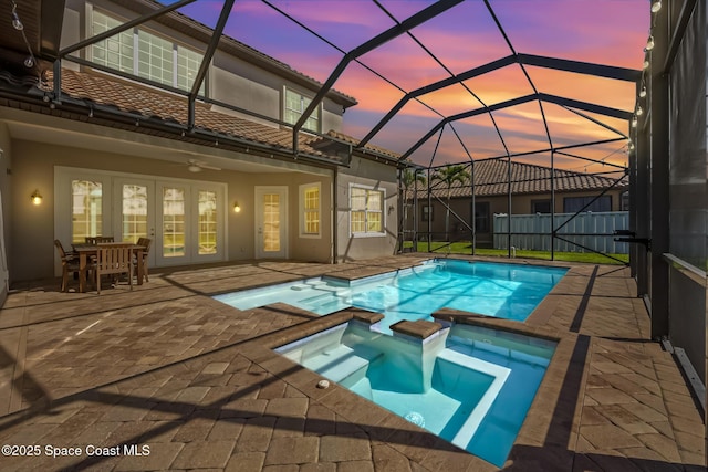 pool at dusk featuring a lanai, a pool with connected hot tub, a ceiling fan, french doors, and a patio area