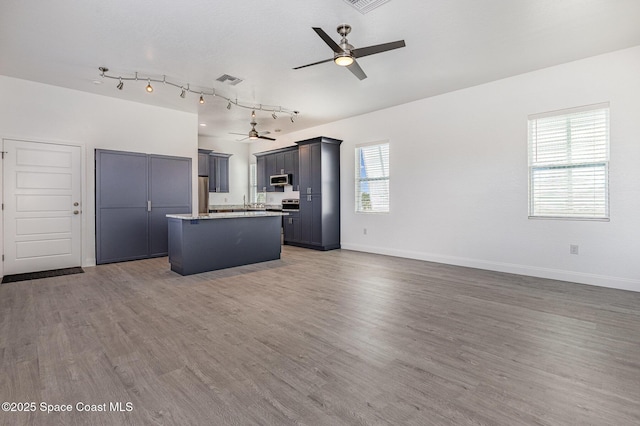 kitchen featuring wood finished floors, a kitchen island, a ceiling fan, open floor plan, and stainless steel microwave