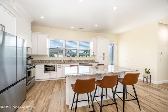 kitchen featuring stainless steel appliances, light wood-style floors, white cabinets, a kitchen island, and a kitchen bar