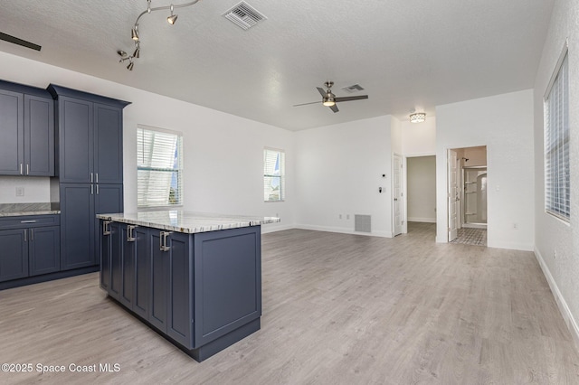 kitchen featuring a textured ceiling, a kitchen island, visible vents, and light wood-style floors