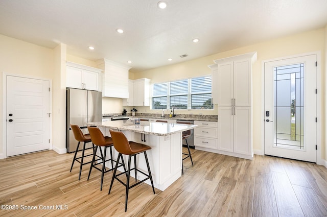 kitchen with white cabinets, a center island, stainless steel appliances, light wood-type flooring, and a kitchen bar