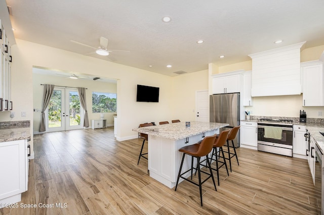 kitchen with light wood-style flooring, appliances with stainless steel finishes, a breakfast bar area, custom exhaust hood, and french doors