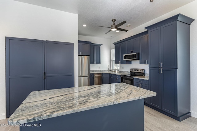 kitchen with ceiling fan, a textured ceiling, light stone counters, appliances with stainless steel finishes, and light wood-type flooring