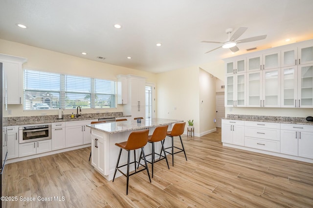 kitchen with light wood-type flooring, a kitchen breakfast bar, white cabinets, and a center island