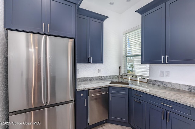 kitchen with appliances with stainless steel finishes, a sink, light stone counters, and blue cabinetry