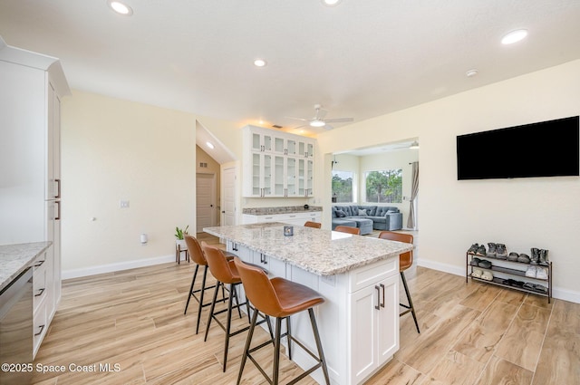 kitchen with light wood finished floors, a kitchen island, a breakfast bar, white cabinetry, and stainless steel dishwasher