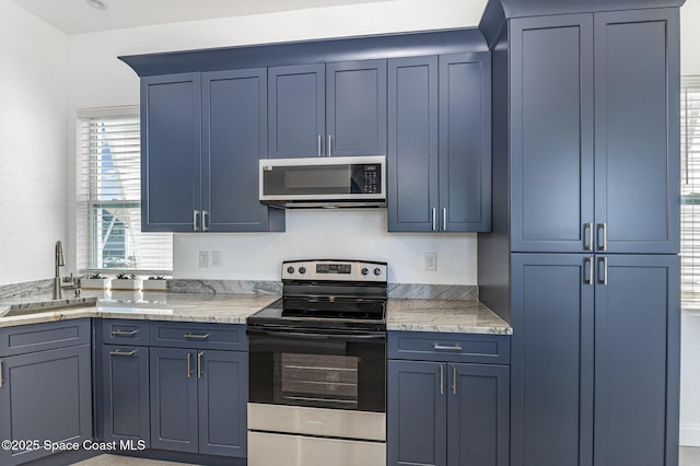 kitchen featuring stainless steel appliances, light stone counters, blue cabinetry, and a sink