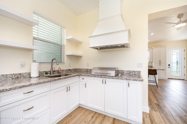 kitchen with premium range hood, open shelves, a sink, and light wood-style flooring