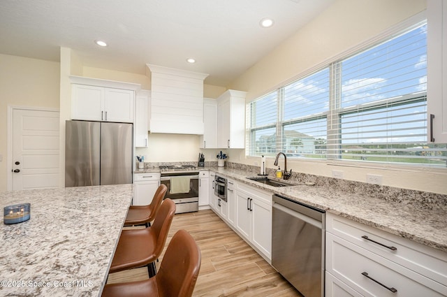 kitchen featuring light wood-style flooring, premium range hood, a sink, white cabinetry, and appliances with stainless steel finishes